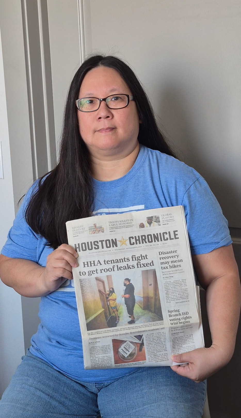 Faye Ku, seated, holds a newspaper reporting the damage to her apartment complex in Houston.