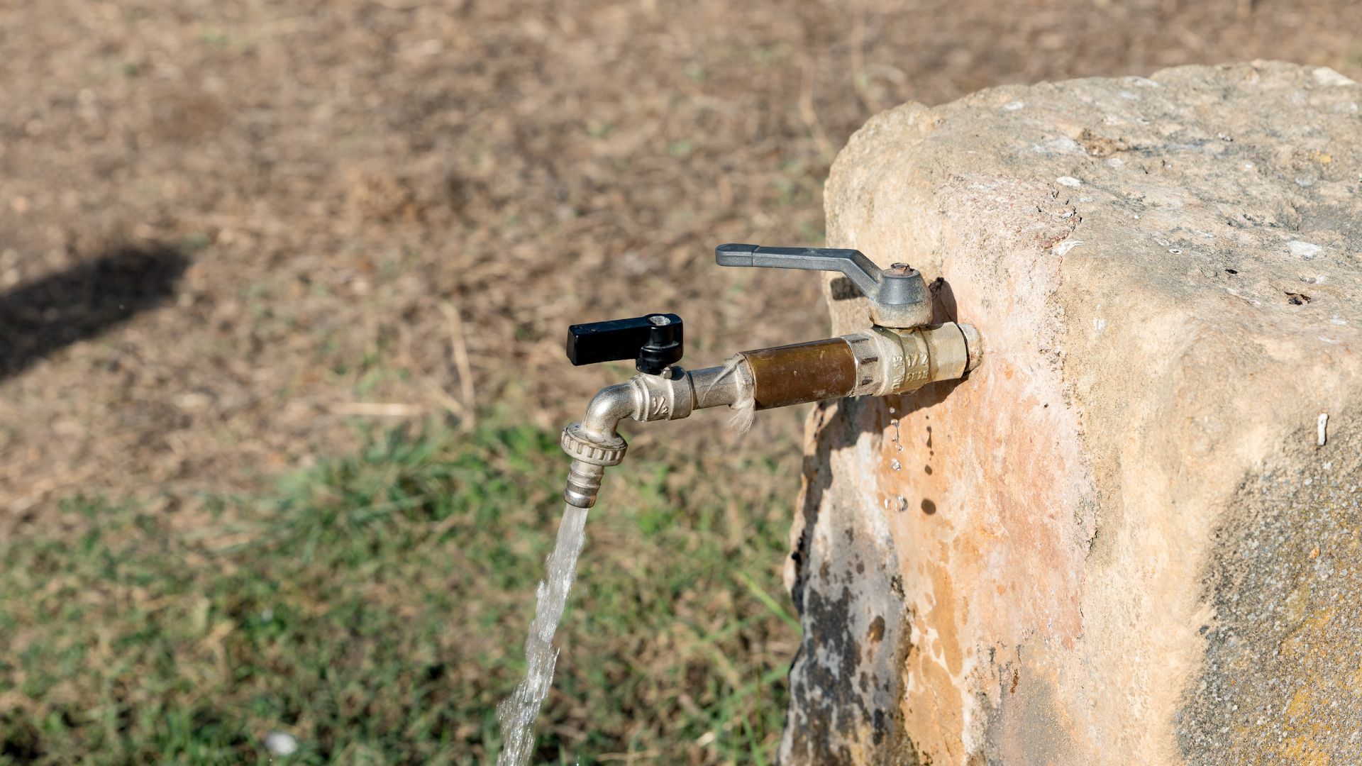 An outdoor water spigot with clear water flowing out of it