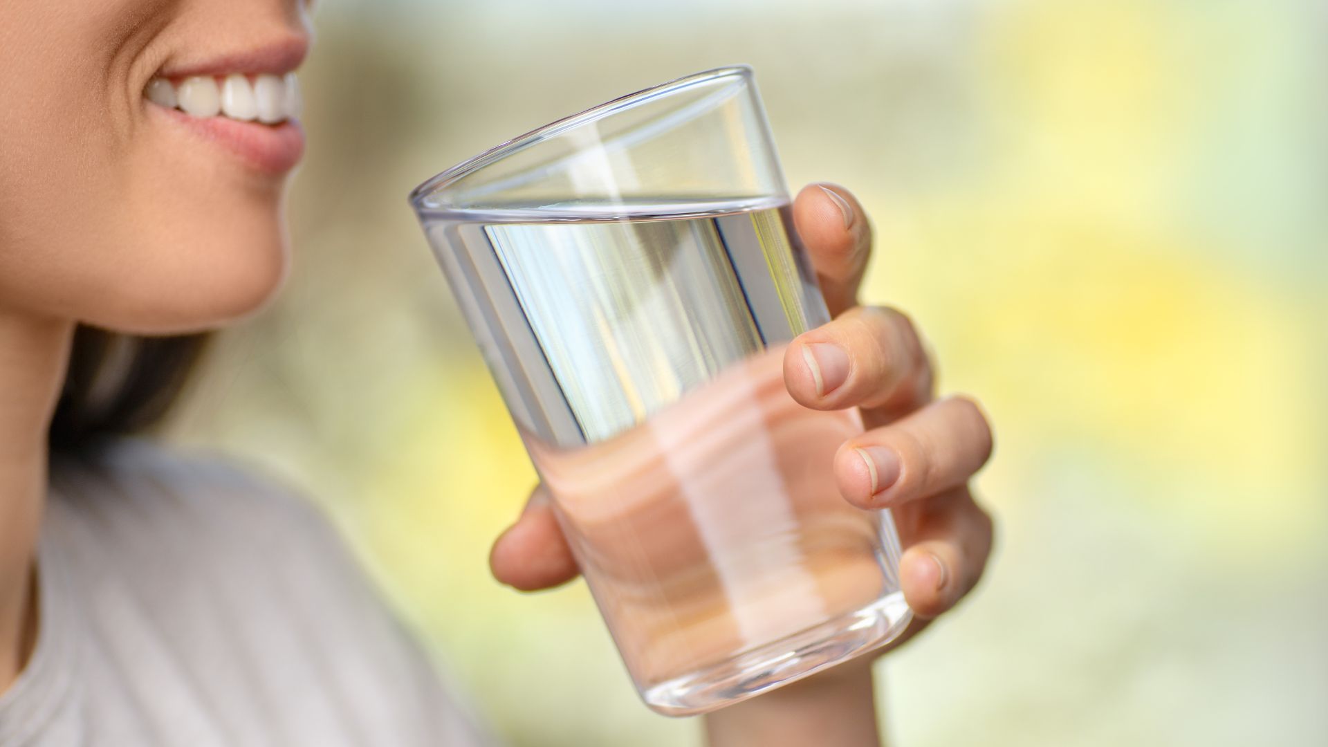 A person smiling as they're about to take a drink from a glass of crystal clear water