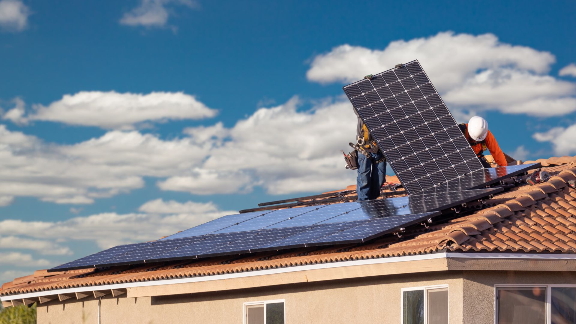 A house with workers actively installing solar panels on the roof