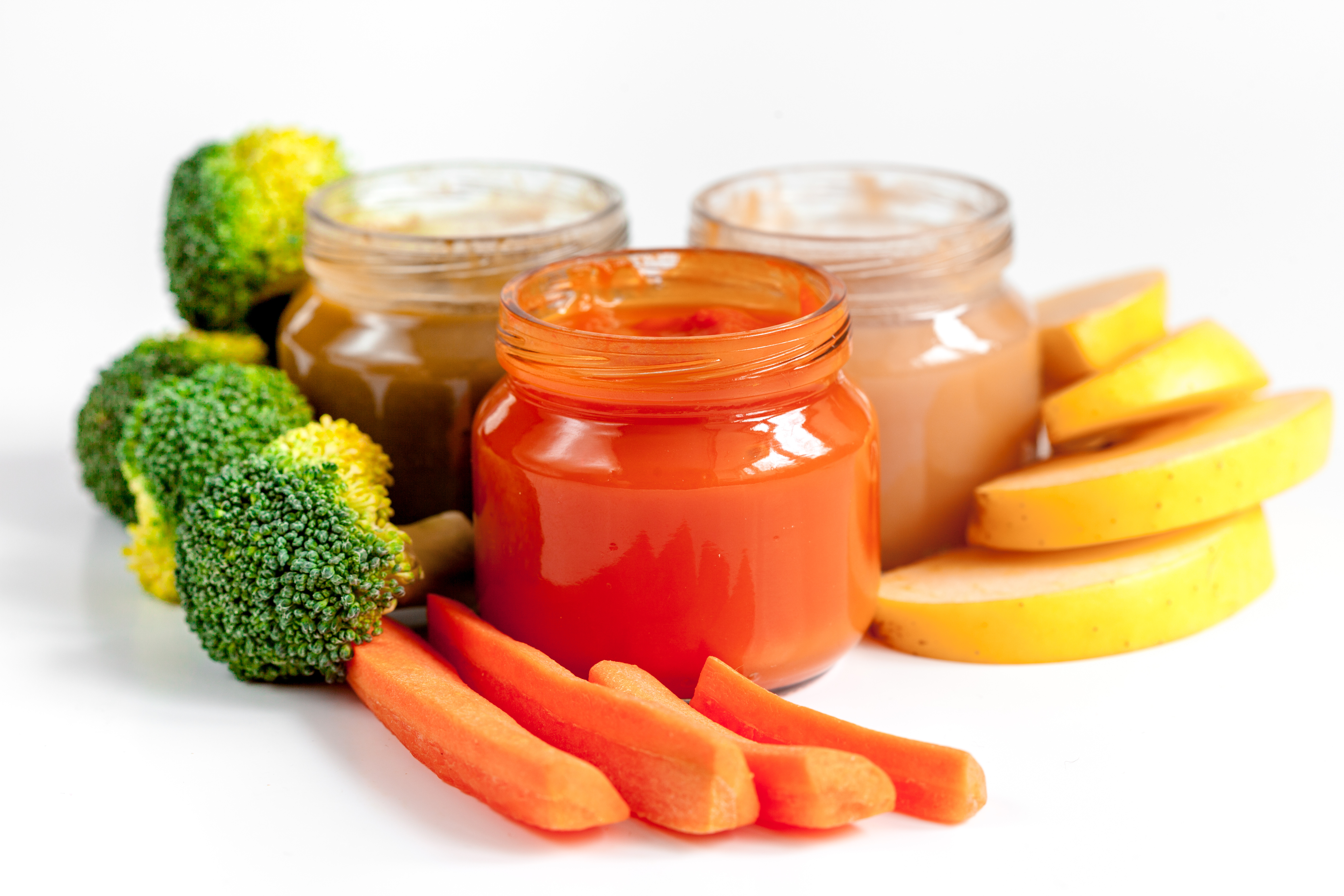 Three jars of baby food surrounded by cut-up vegetables and fruit
