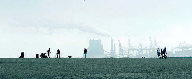 people in a field with smokestacks in the distance