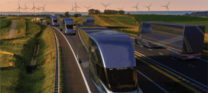 Row of trucks driving on freeway with windmills in the distance