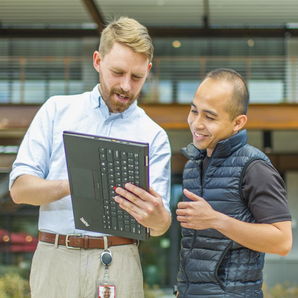 Two people in conversation outdoors, working on a tablet.