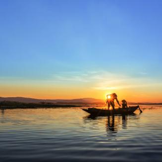 Fishers on a fishing boat on the water with sunset