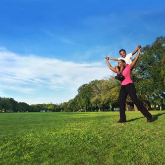 Mother with child on her shoulders in a field under a blue sky