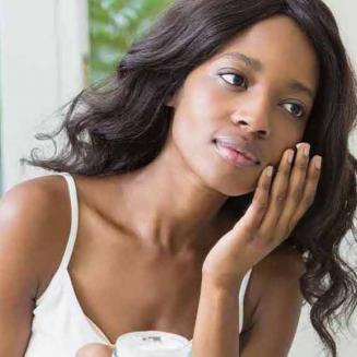 Black woman applying lotion to her face