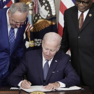President Joe Biden signs the Inflation Reduction Act while Senator Chuck Schumer and Representative Jim Clyburn look on