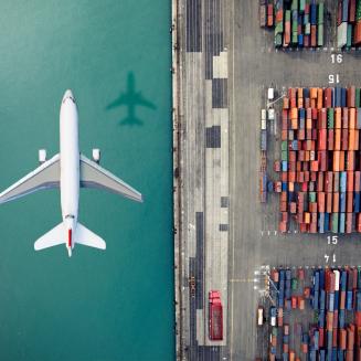 A plane flying over a dock, half of the ground is water and half is shipping containers