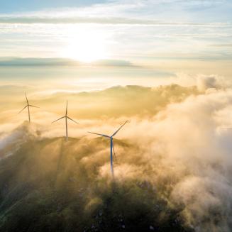 A soaring shot of wind turbines bathed in clouds at sunrise