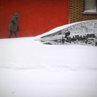 People trekking past a car which is covered to the hood in snow