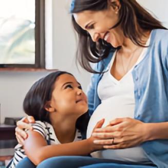 Pregnant mom smiling at a child who is touching her belly