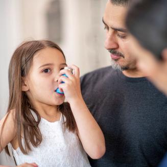 Girl using an asthma inhaler as adults look on