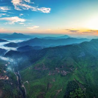 Vibrant scenery featuring tree-covered mountains viewed from overhead at sunrise or sunset.