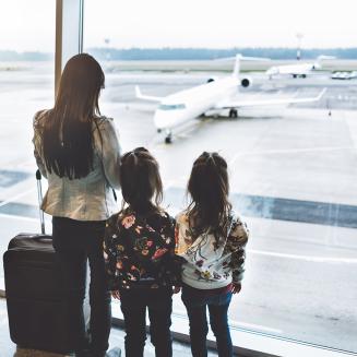 A caregiver with two kids looking out of an airport window at airplanes.