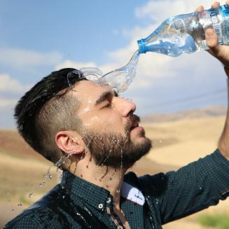 Man pouring a bottle of water into his face in front of a desert background