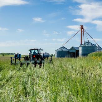 a tractor drives through a grain field toward grain storage towers