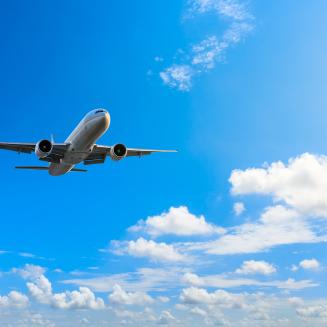 White plane flying in a blue sky with scattered clouds