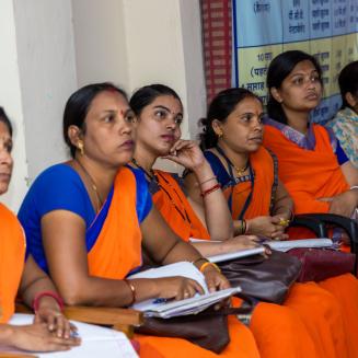 Line of women in saris listening to a presentation. They are India's accredited social health activists (ASHAs) being trained on the health issues caused by air pollution. Photo by Megha Namdeo