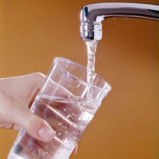 Hand holding a glass of water below a chrome faucet spigot