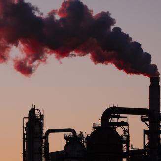 An industrial facility at sunset with billowing smoke coming out of it.