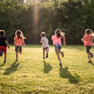 Back view children running together in public park at sunset