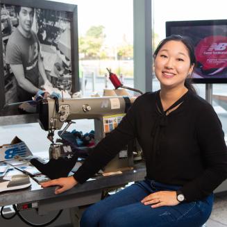 A former Climate Corps fellow inside a brightly lit building, with a screen displaying the New Balance logo.