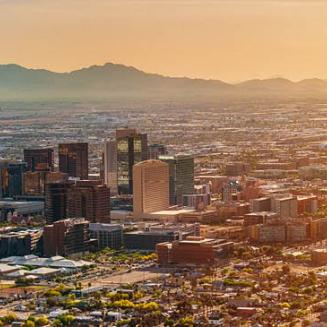 Panoramic view of Arizona city skyline with mountains in background and yellow sun at right