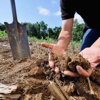 Person kneeling on the ground with dirt in their hands and a shovel nearby