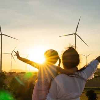 Woman and child with arms extended look at wind turbines as the sun sets
