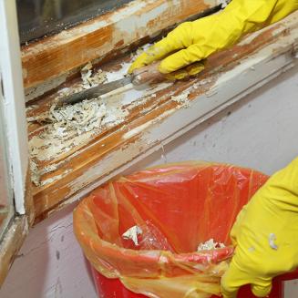 Close view of gloved hands scraping paint from a window sill
