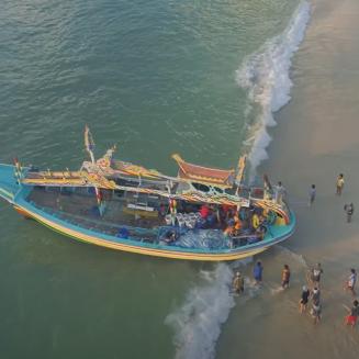 People walk along a beach to meet a fishing boat coming ashore.