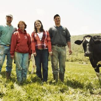 Group of four standing next to a cow on a farm