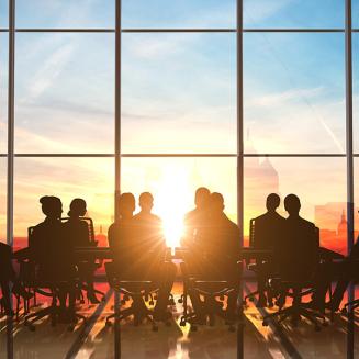 Collection of business people sitting at a table in front of the sunset.