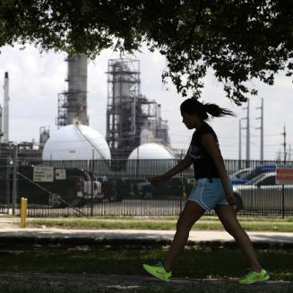 A teenage girl walks by a Houston oil refinery, one of many industrial facilities contributing to the city's pollution problem.