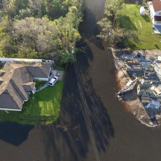Aerial view of a coastal house destroyed by extreme weather, beside an intact house.