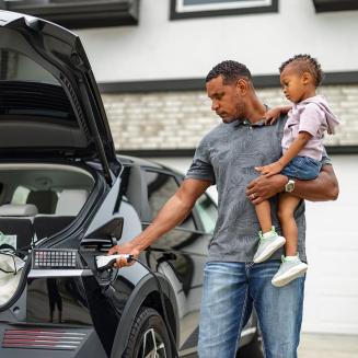 A dad holding a kid while plugging in an electric vehicle.