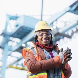 Woman wearing a hard hat, safety vest and safety goggles, working at a shipping port.