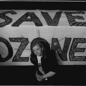 A person sitting in front of a "save ozone" sign.