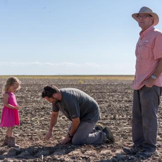 Dwane Roth standing next to his nephew Zion as he digs in the soil. His young daughter stands next to him.