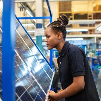 Side view of a female employee inspecting newly manufactured solar panels in company. Woman quality engineer examining solar panels in factory.