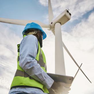 Worker in bright blue hard hat standing beneath a wind turbine.