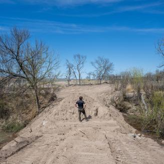 A man surveys water flow from a dusty road.