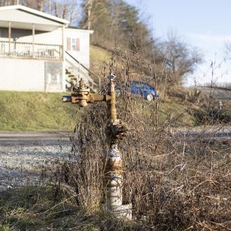 A rusty pipe sticking out of the ground with a house and car in the near background.