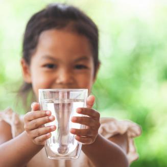 A little girl holds up a glass of drinking water.