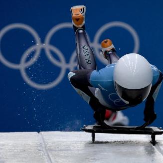 Katie Tannenbaum hopping onto a skeleton sled with the Olympics rings behind her.