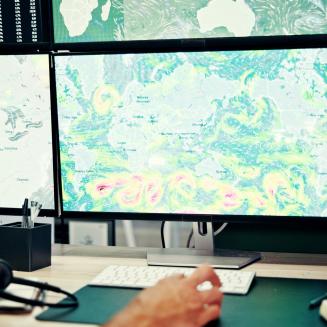 Four computer screens showing various maps and data.