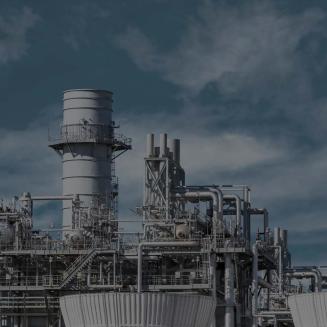 Industrial power generation facility with large metal stacks, pipes, platforms, and cooling structures under a cloudy blue sky.
