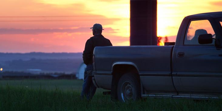 Man overlooking sunset while leaning on pick up truck.