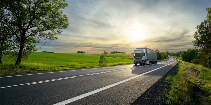 A truck driving down a highway next to a beautiful open field.